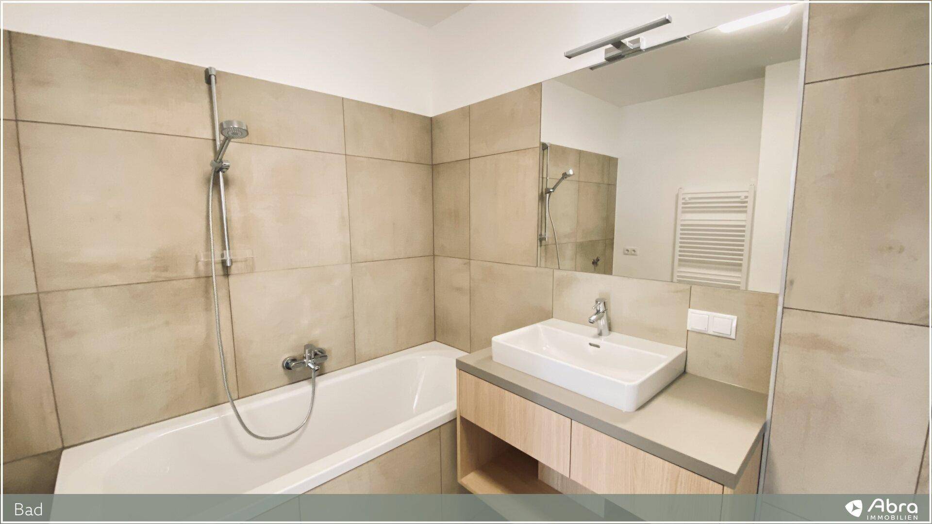 Helles Badezimmer mit Badewanne, modernem Waschtisch und großem Spiegel, sowie Handtuchheizkörper.