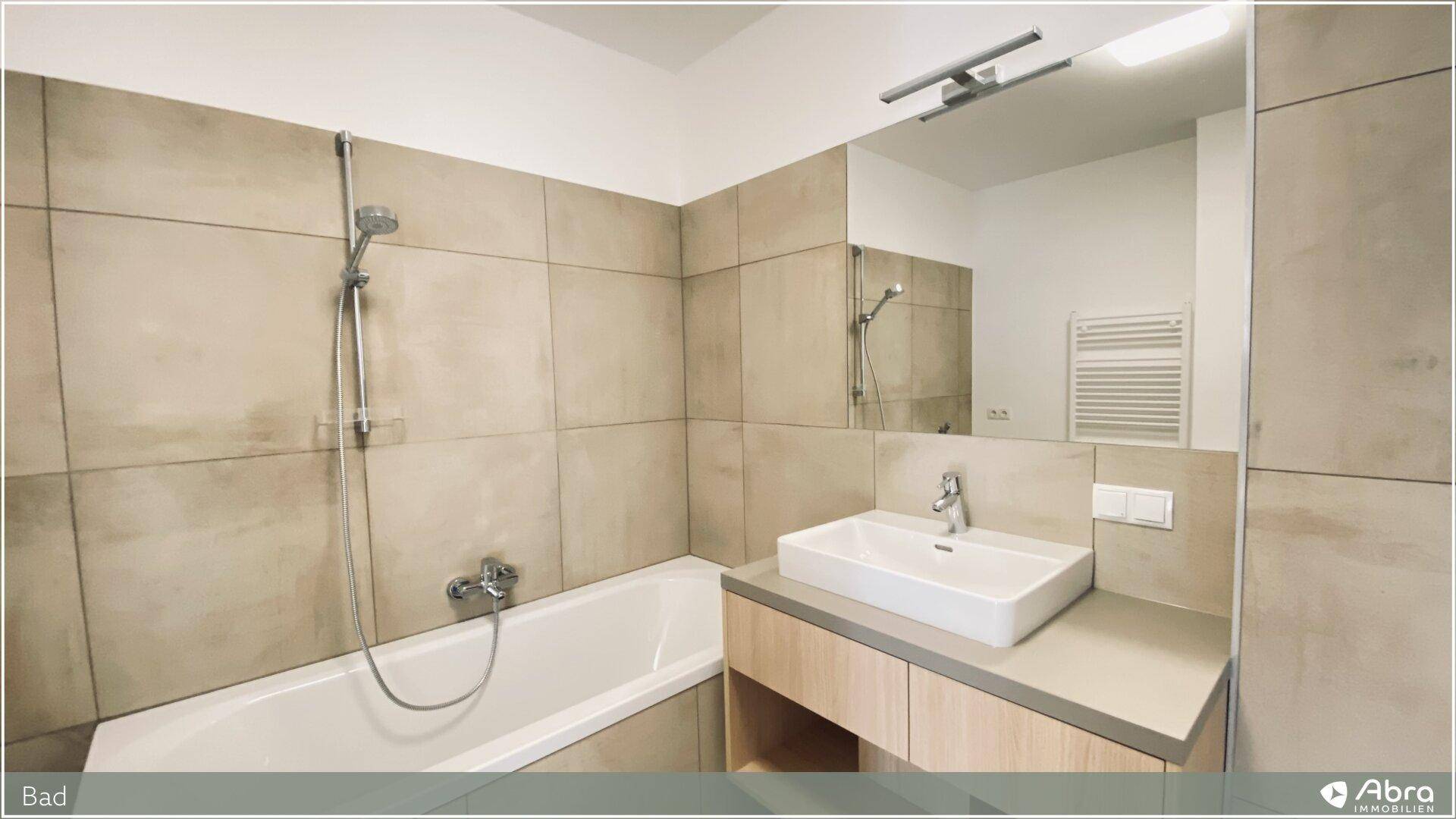 Modernes Badezimmer mit Badewanne, Waschtisch und Spiegel, in neutralen Farbtönen gehalten.