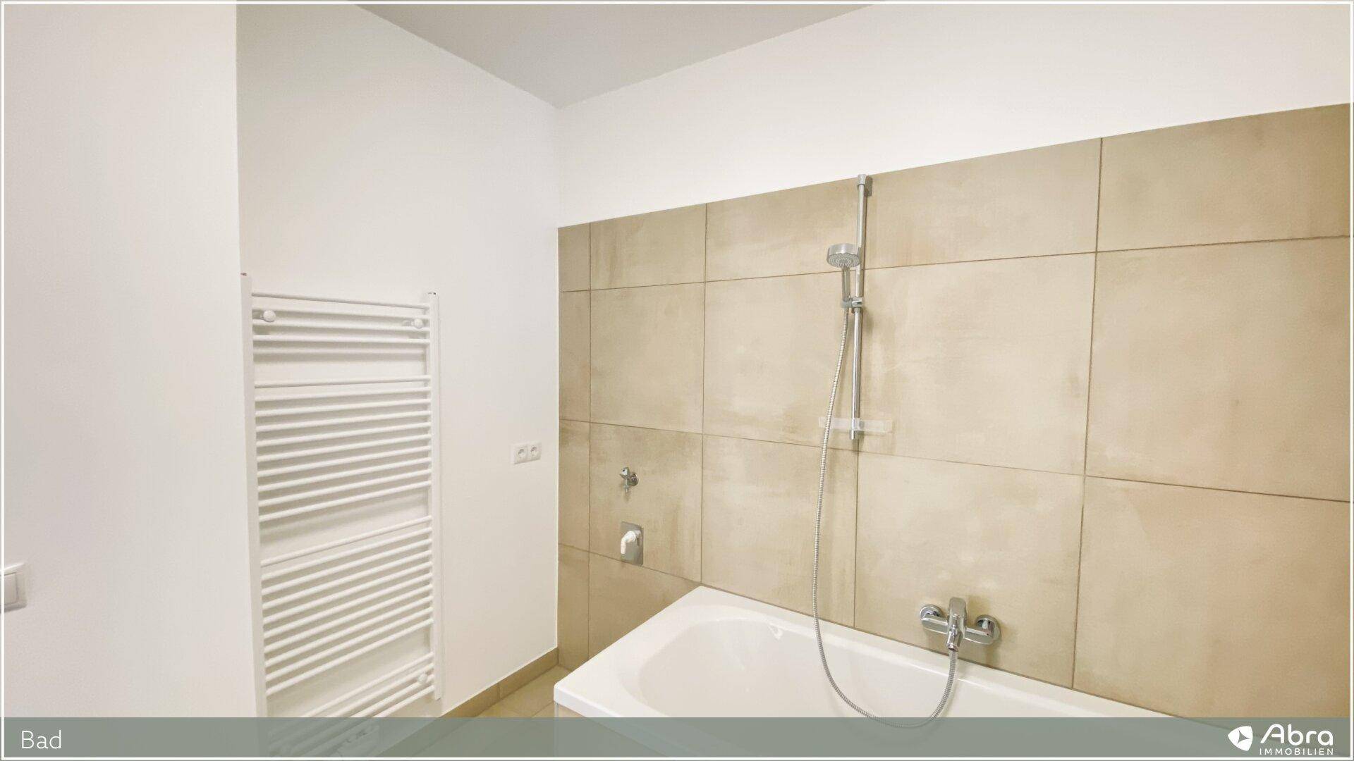 Badezimmer mit Badewanne und beheiztem Handtuchhalter, gefliest in warmen Beigetönen.