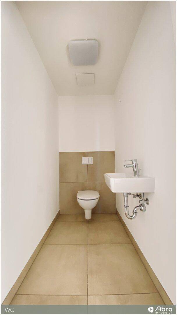 Separates Gäste-WC mit wandhängender Toilette und kleinem Handwaschbecken, gefliest.