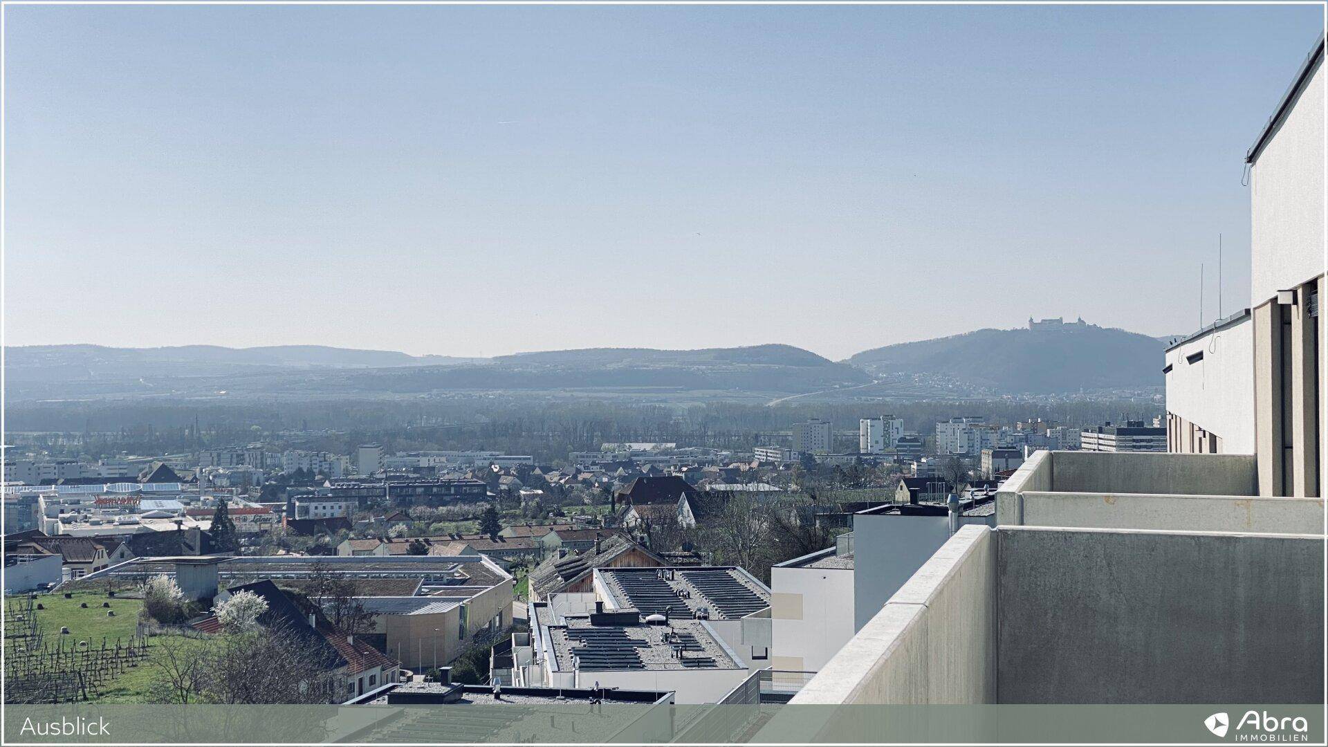 Panoramablick über eine Stadt mit hügeliger Landschaft und Bergen im Hintergrund.