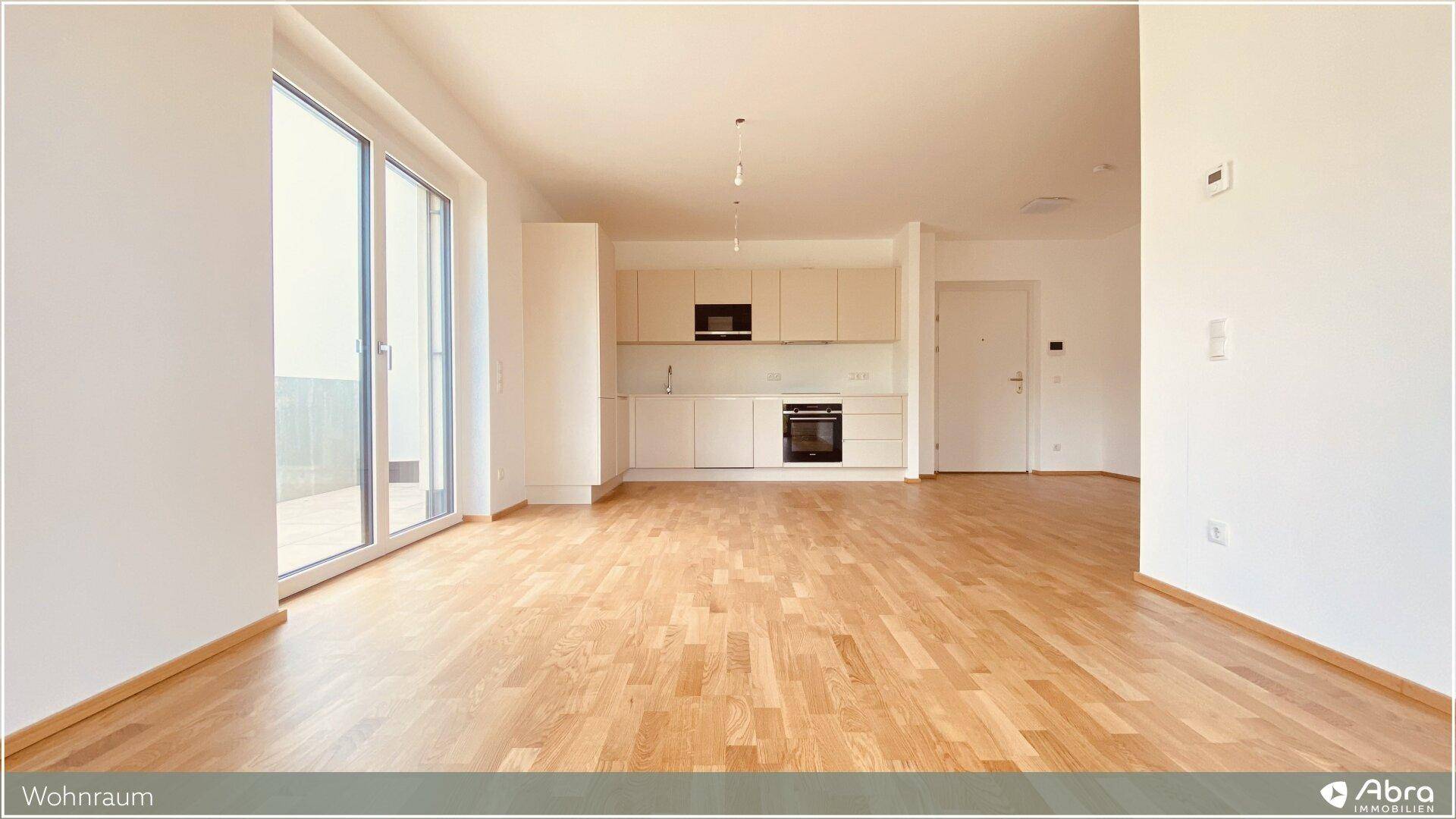 Moderner Wohnbereich mit heller Einbauküche, Holzboden und großem Fenster zum Außenbereich.