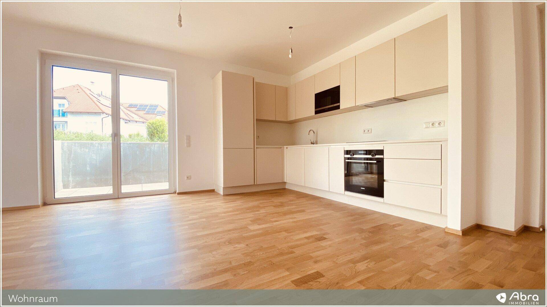 Heller Wohnbereich mit integrierter Küche, Holzboden und Zugang zu einem sonnigen Balkon.