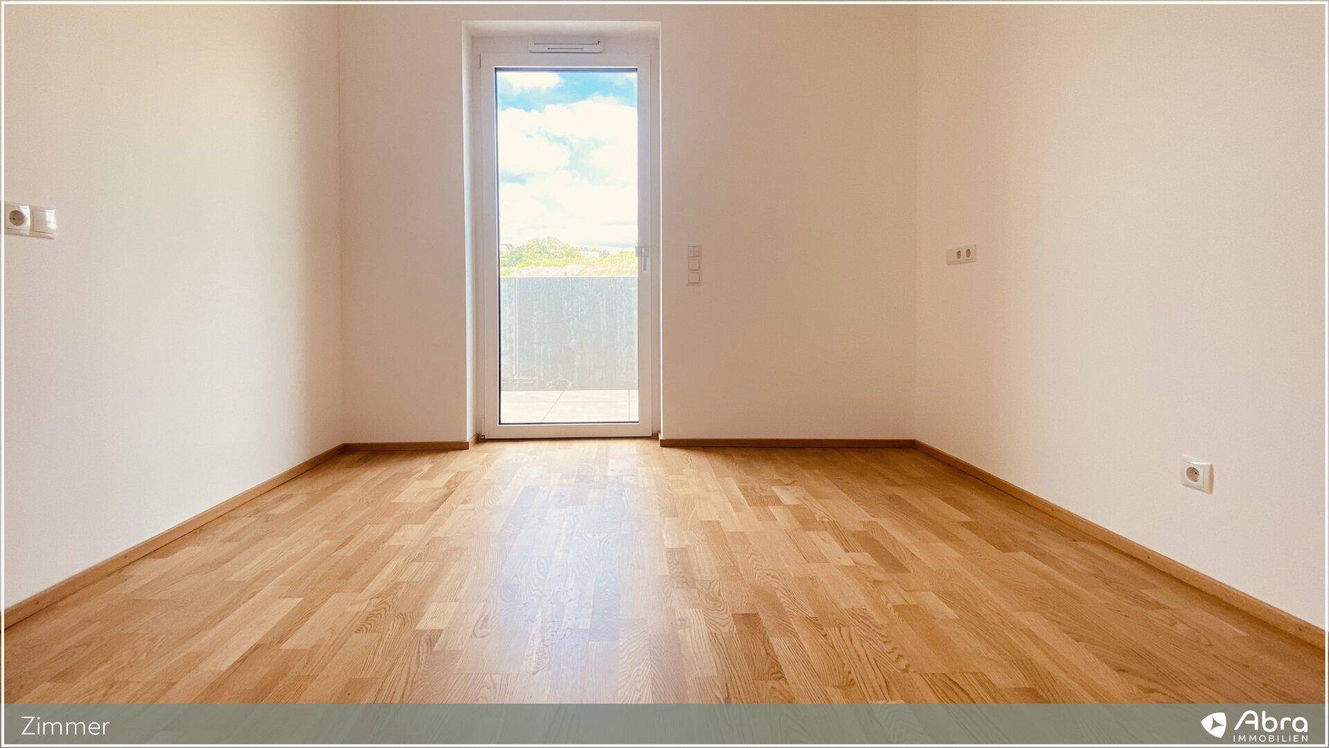 Helles Zimmer mit Holzboden und Zugang zu einem Balkon oder einer Terrasse.