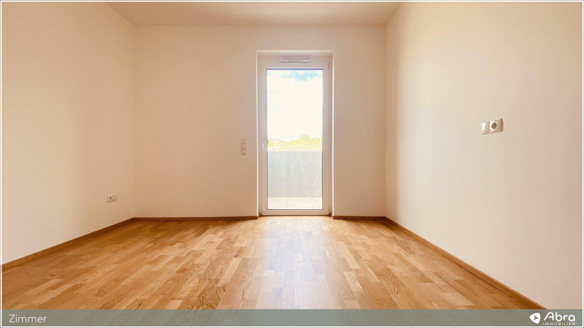 Geräumiges Zimmer mit Parkettboden und viel Tageslicht durch die Balkontür.