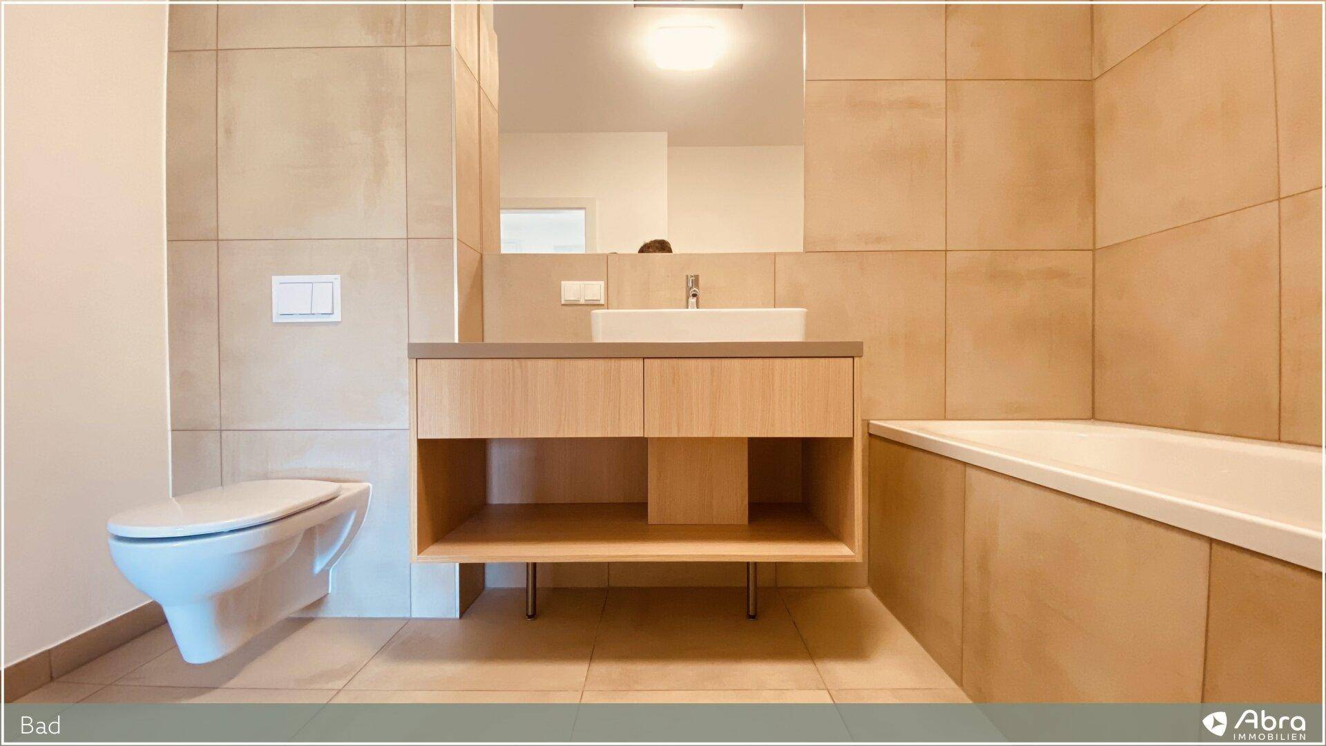 Modernes Badezimmer mit Wand-WC, Waschtisch und integrierter Badewanne, komplett gefliest.