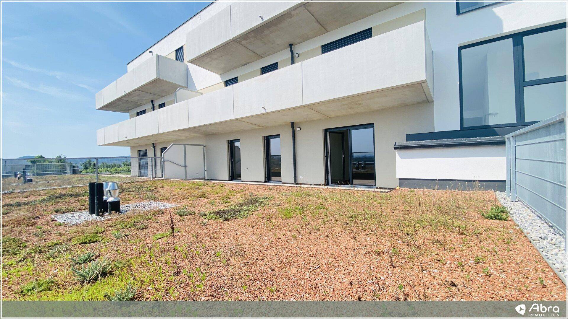 Moderne Gebäudefassade mit großen Fenstern und einer weitläufigen, begrünten Terrasse.