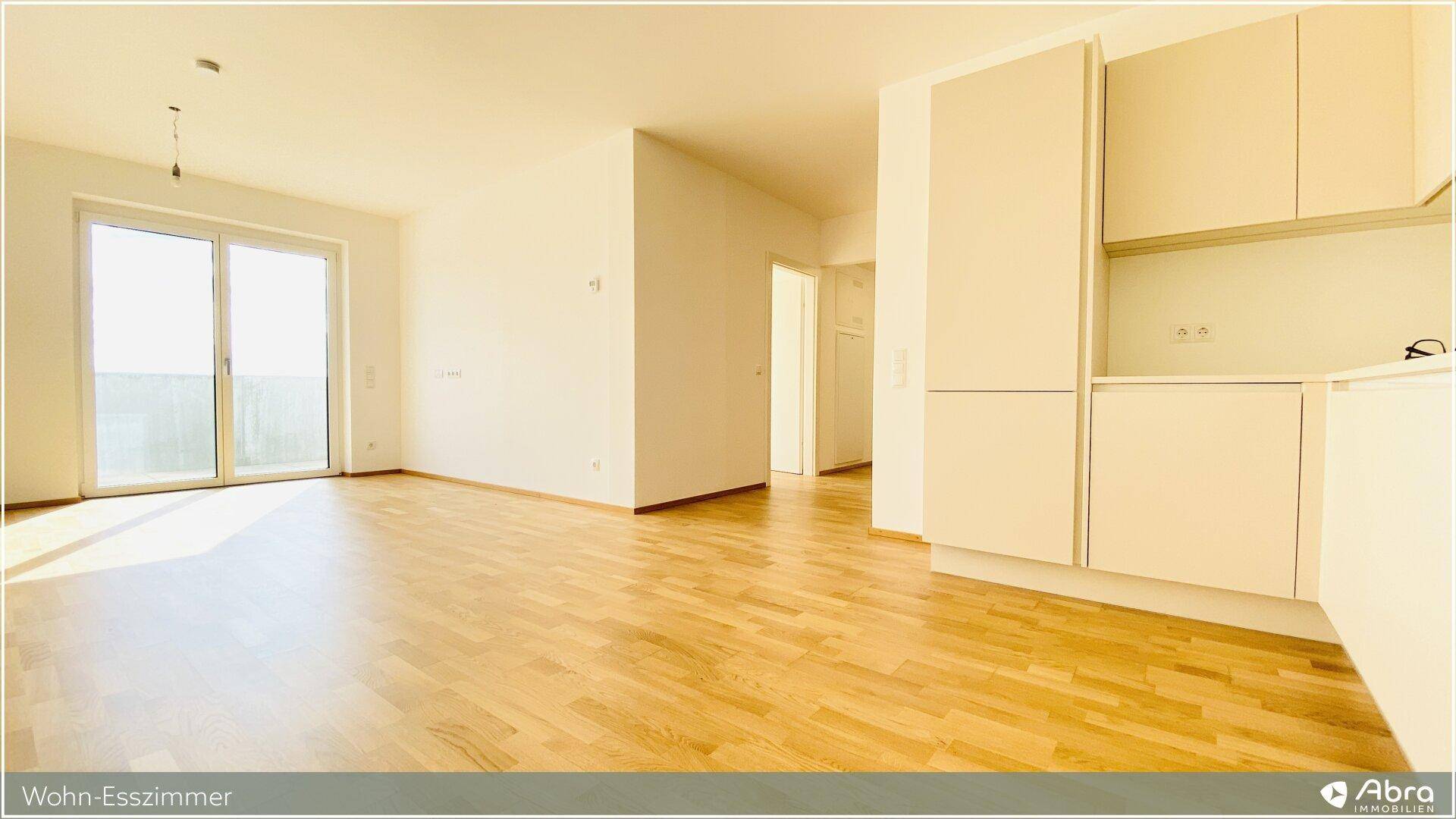 Sonniger Wohn-Essbereich mit hellem Holzparkett und Zugang zum Balkon, ideal für offenes Wohnen.
