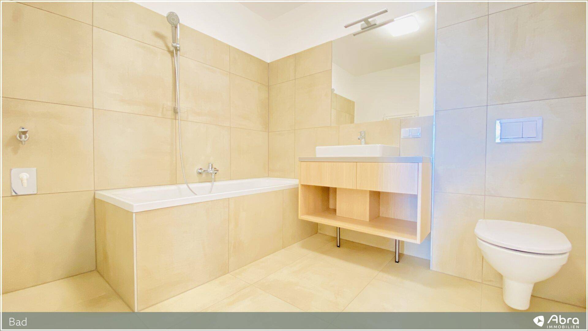 Helles Badezimmer mit Badewanne und modernem Waschtisch, ausgestattet mit beigen Fliesen.