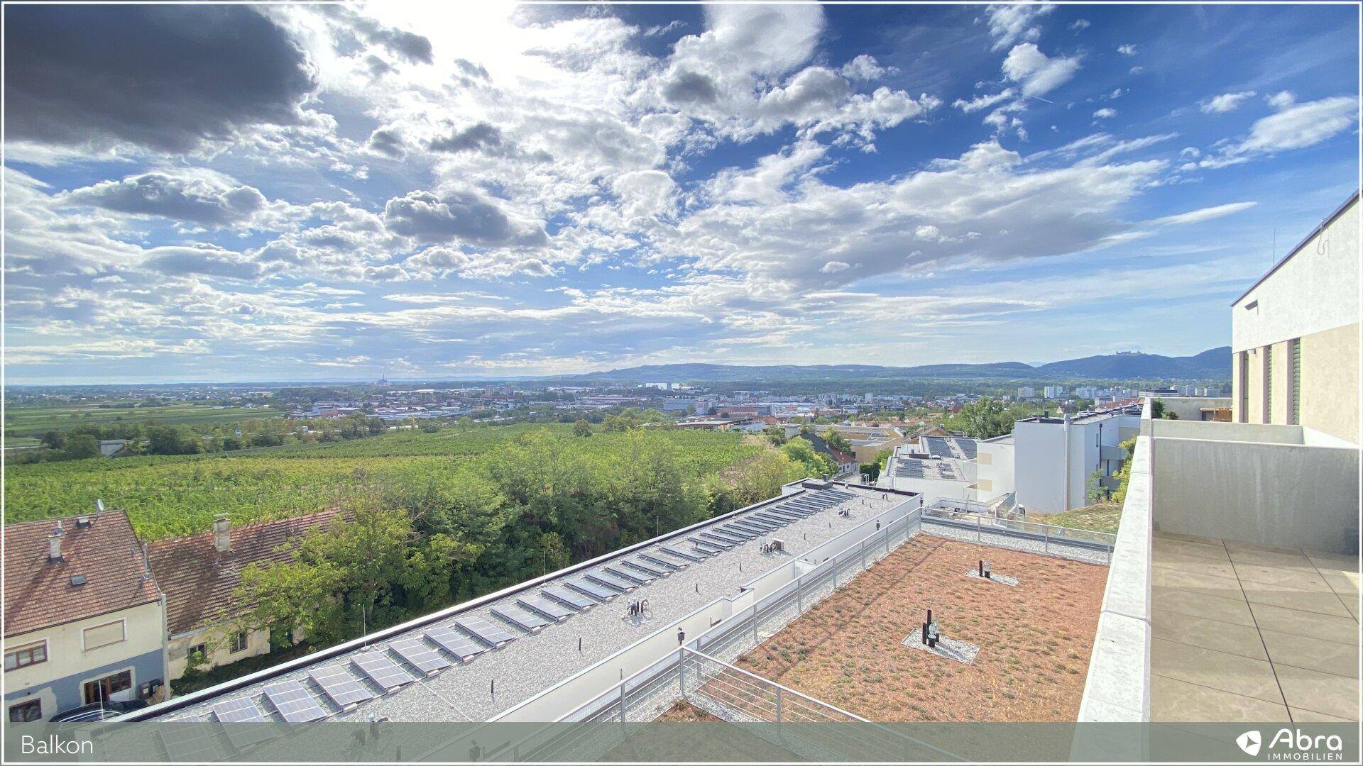 Großer Balkon mit weitem Blick über die Landschaft und die Stadt, inklusive Solaranlage auf dem Dach.
