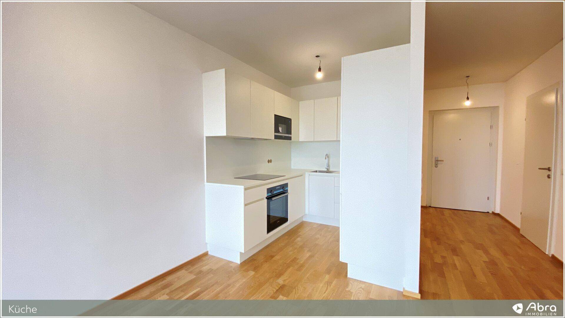 Moderne Küchenzeile mit integriertem Backofen und Induktionskochfeld in hellem Design und Holzfußboden.
