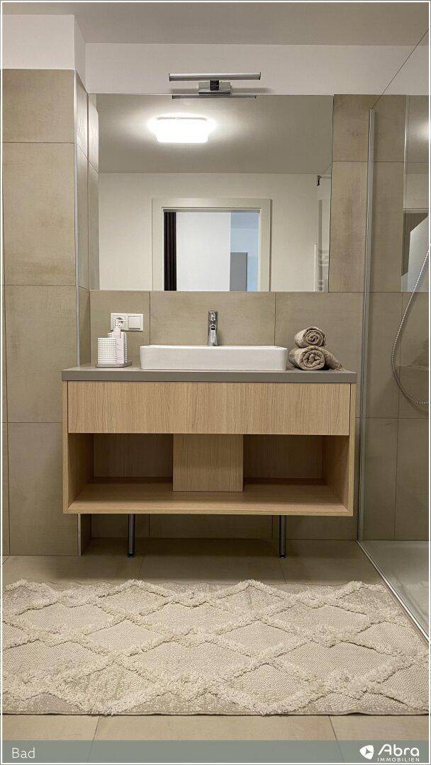 Detailaufnahme des modernen Einzelwaschbeckens mit Holzunterschrank und großem Spiegel im Badezimmer.