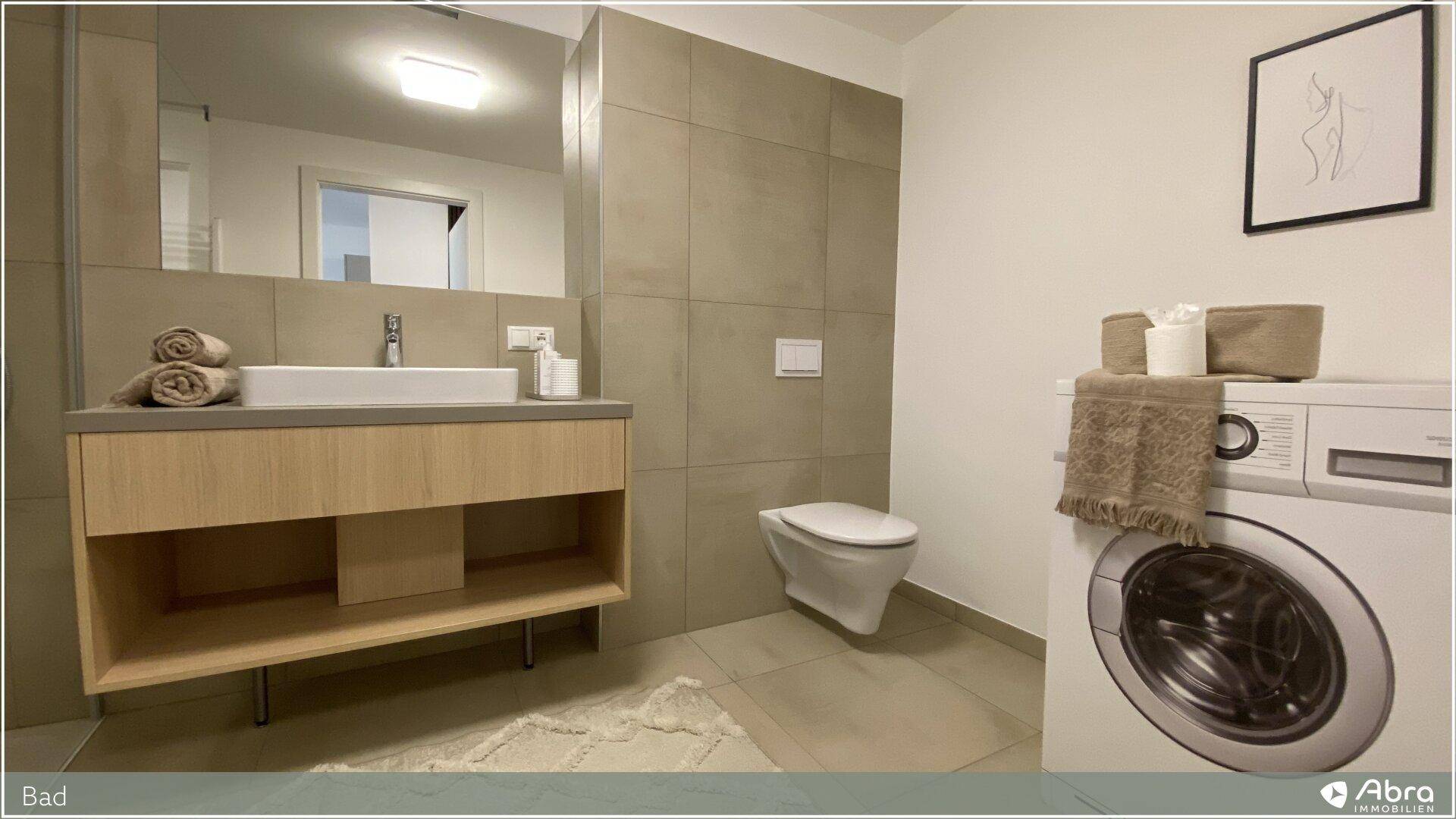 Helles Badezimmer mit wandhängendem WC und integrierter Waschmaschine, modern gefliest und funktional.