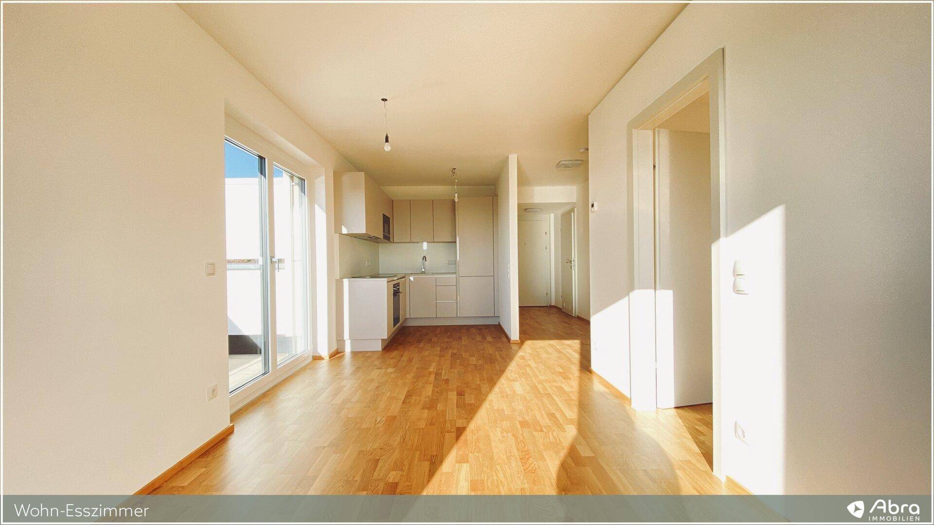 Offener Wohn-Essbereich mit hellem Parkettboden und Zugang zur Terrasse, angrenzend an eine moderne Küche.