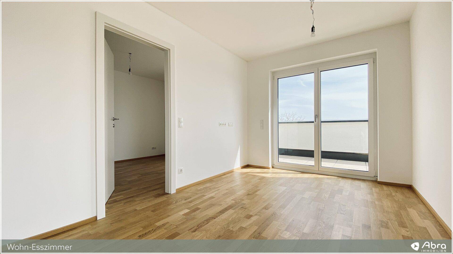 Geräumiger Raum mit Parkettboden und weißen Wänden, mit Zugang zu einem sonnigen Außenbereich.