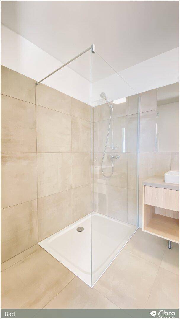 Elegante begehbare Dusche mit Glasabtrennung und großformatigen beigefarbenen Fliesen im modernen Bad.