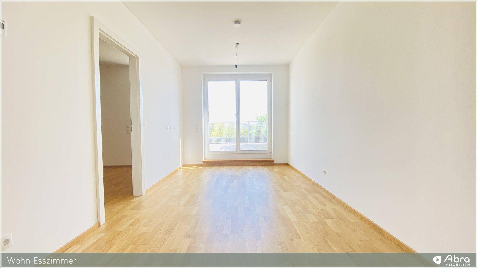 Helles Wohn-Esszimmer mit Holzboden und Zugang zu einem Balkon oder einer Terrasse.