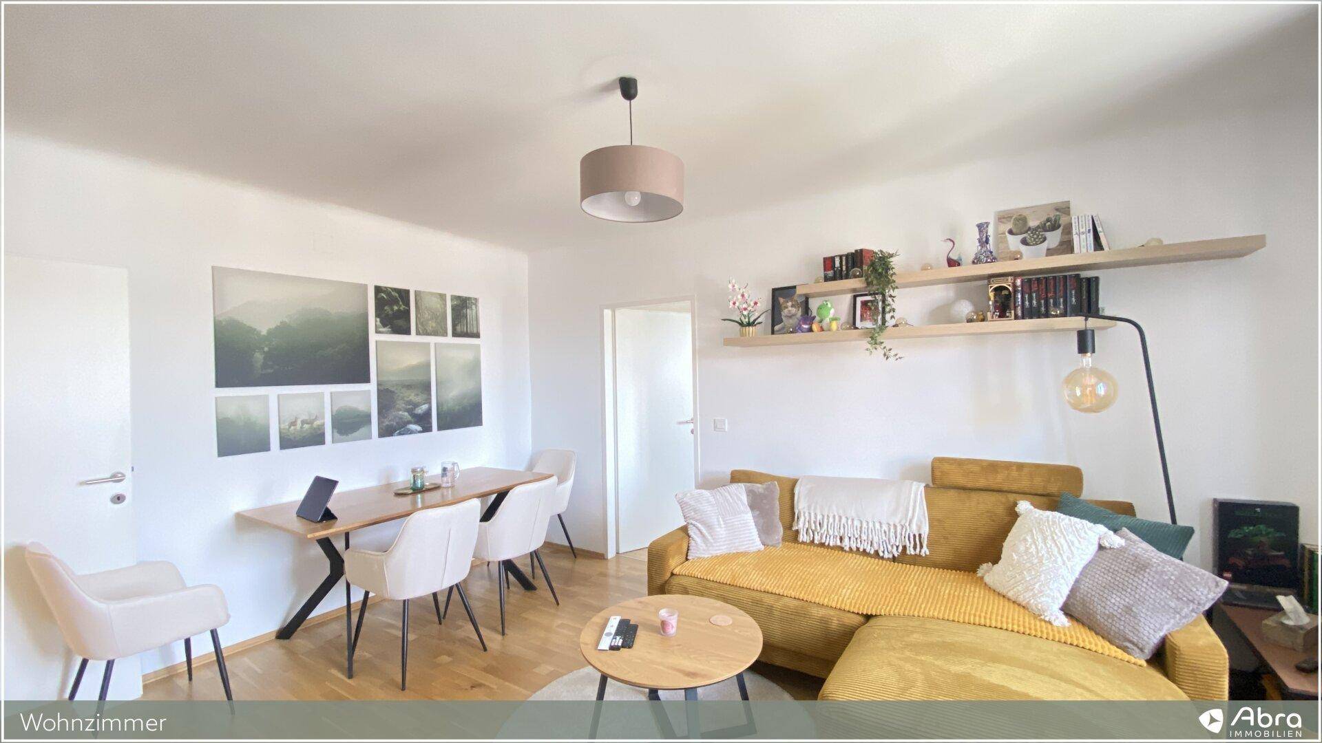 Gemütlicher Wohnbereich mit gelbem Ecksofa, Holzboden und Essbereich, dekoriert mit Wandregalen.