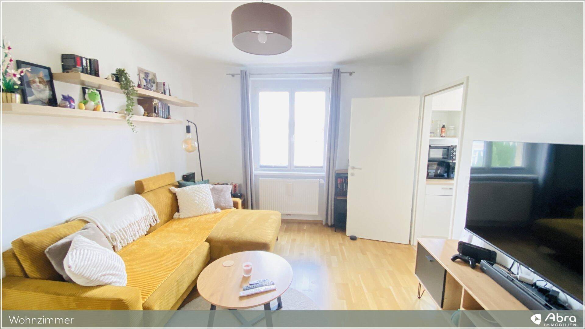 Wohnzimmer mit großem Fenster, gelbem Sofa und TV-Möbel, bietet eine helle und einladende Atmosphäre.