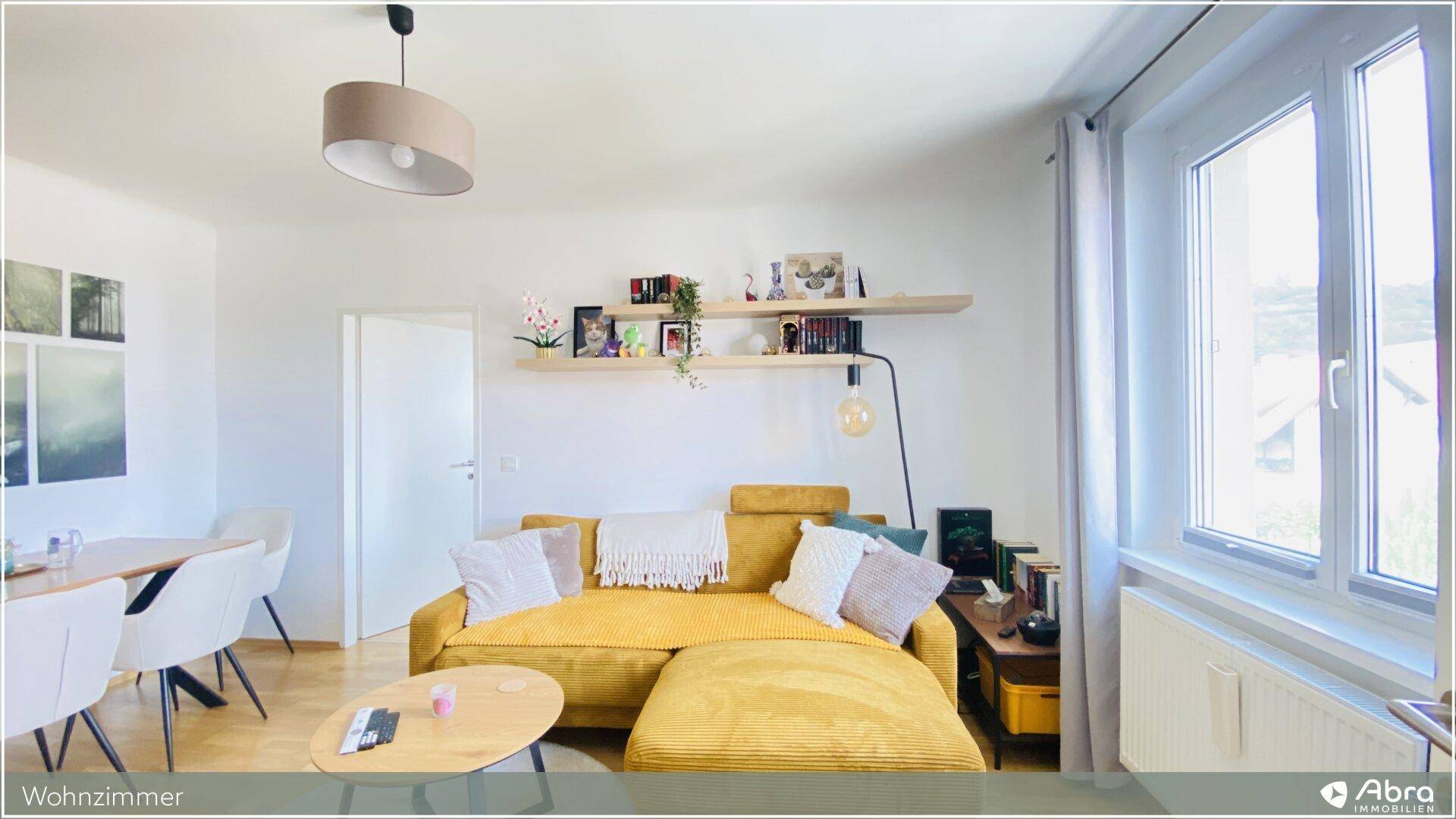 Heller Wohnbereich mit großem Fenster, gelbem Sofa und Essbereich, ideal für entspannte Momente.