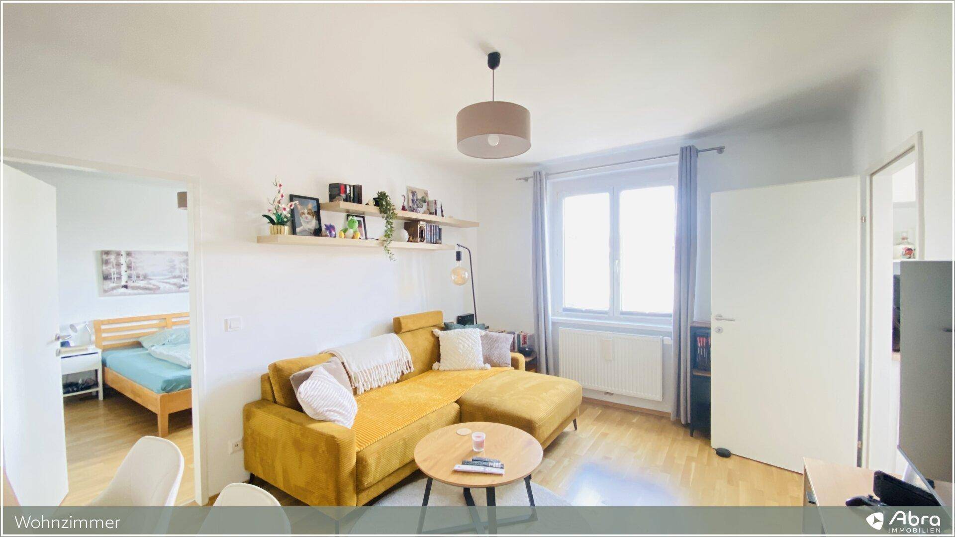 Wohnbereich mit gelbem Sofa und Fenster, bietet einen Blick in ein angrenzendes Schlafzimmer.