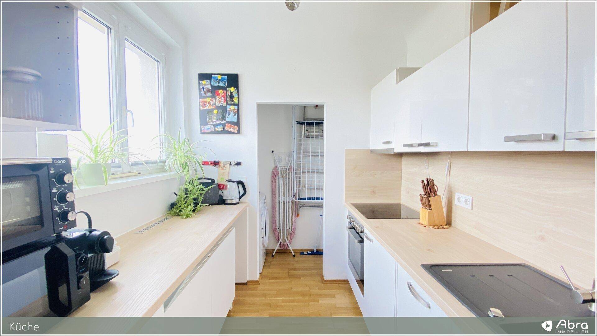Funktionale Küche mit weißen Schränken, Holzarbeitsplatten und Fenster, bietet ausreichend Stauraum.