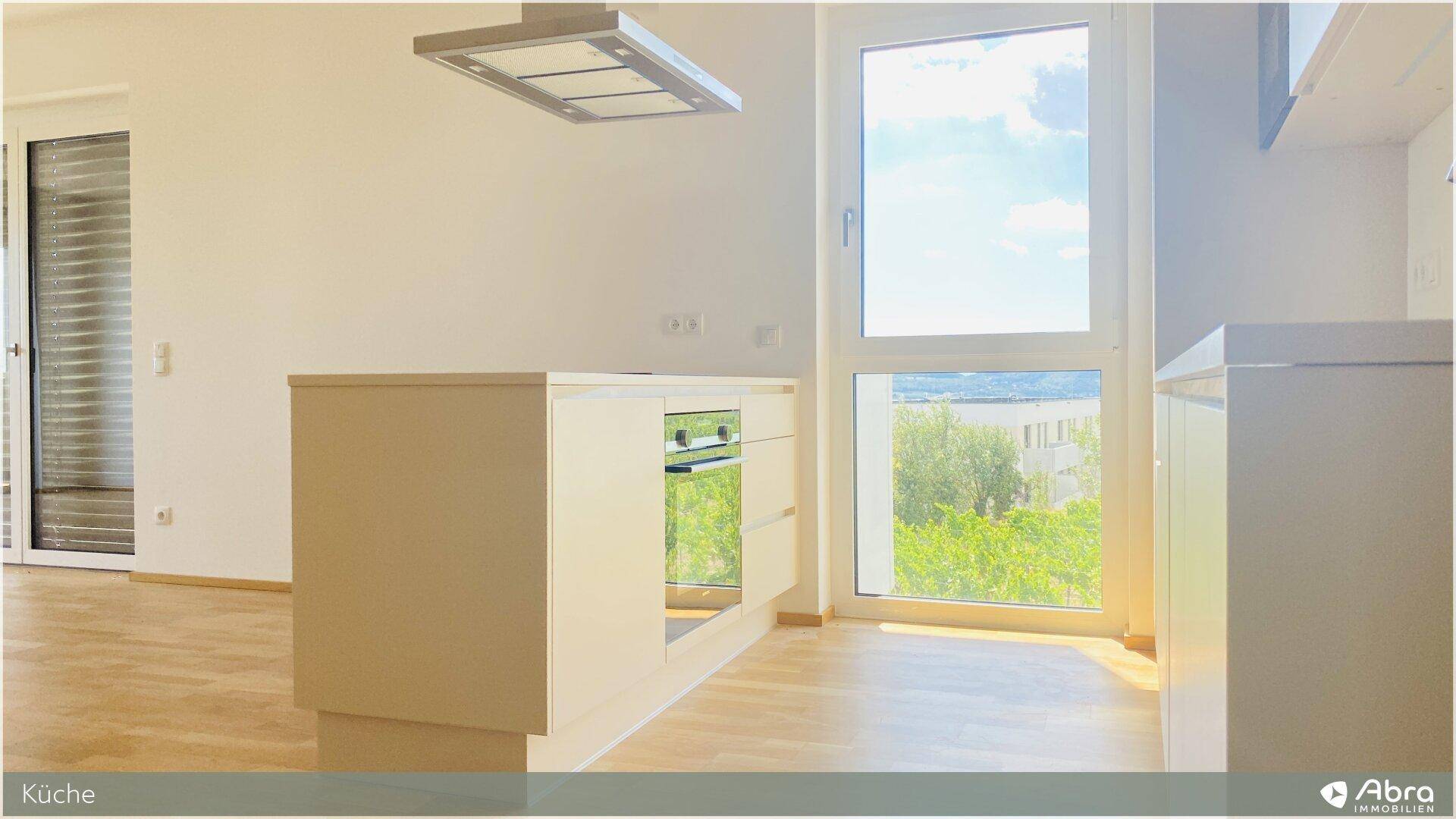 Kücheninsel mit integriertem Backofen und großem Fenster mit Blick ins Grüne.