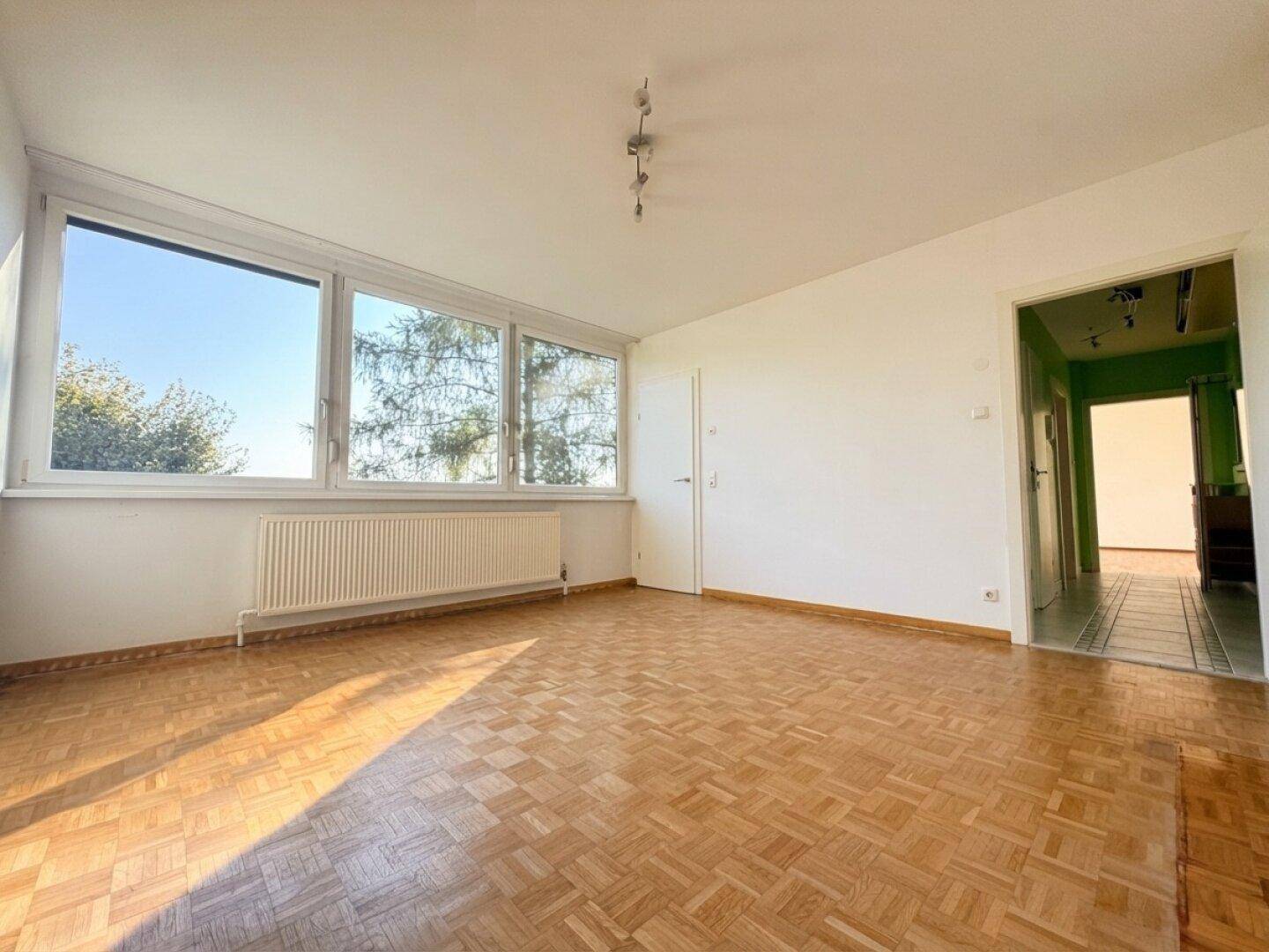 Lichtdurchflutetes Wohnzimmer mit Parkettboden und Zugang zum Flur, ideal für individuelle Gestaltung.