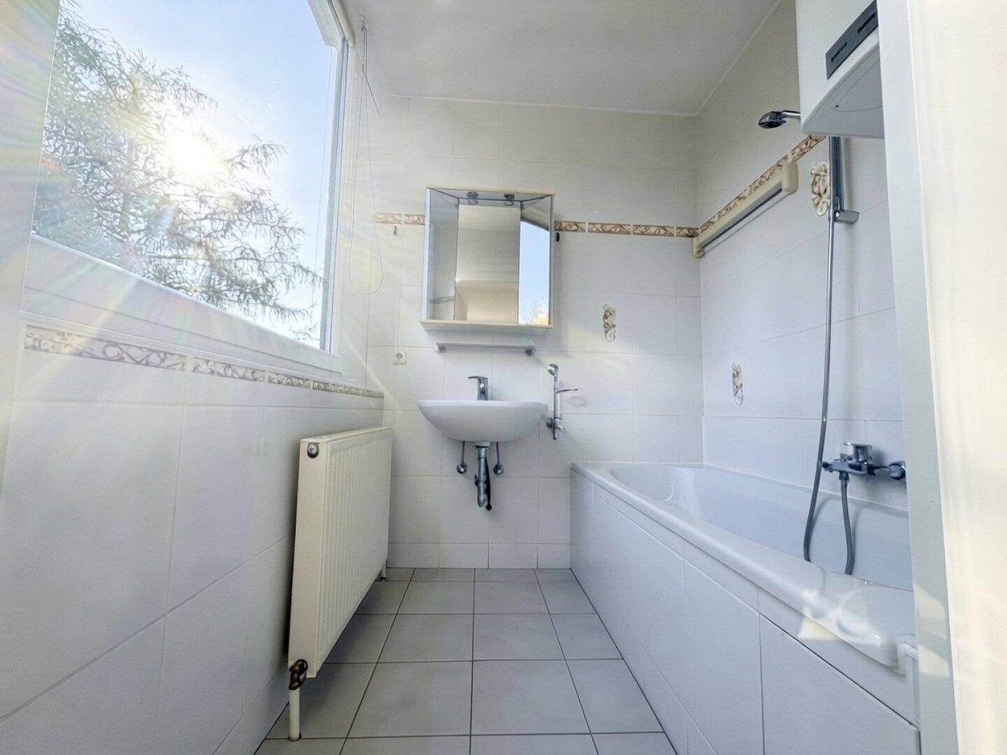 Helles Badezimmer mit Badewanne, Waschbecken, Spiegelschrank und Fenster für natürliche Belüftung.