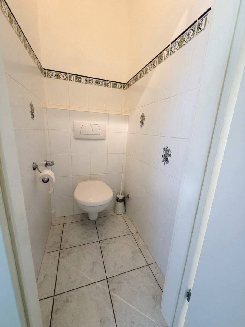 Separates WC mit wandhängender Toilette und weißen Fliesen, praktisch und platzsparend gestaltet.