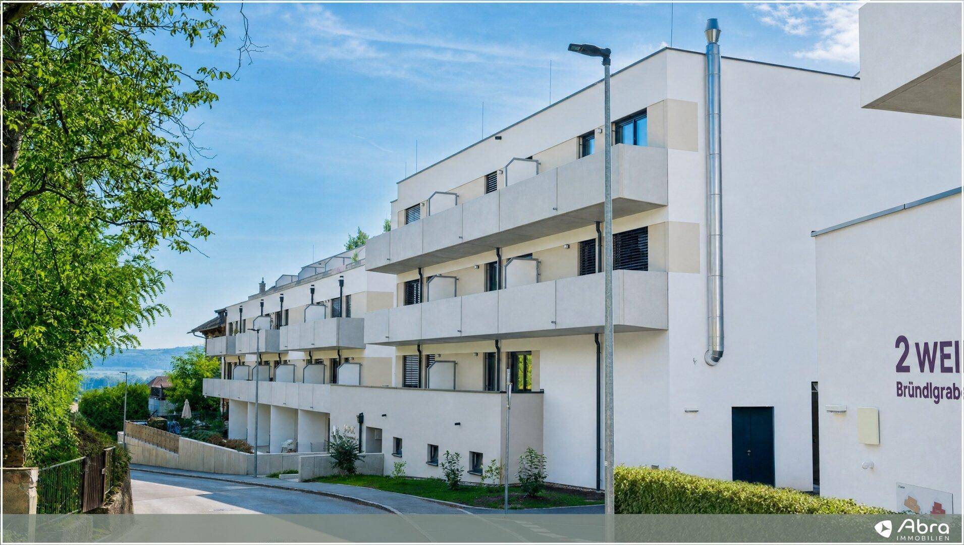 Helle, moderne Wohngebäude mit Balkonen und einer gepflegten Außenanlage unter blauem Himmel.