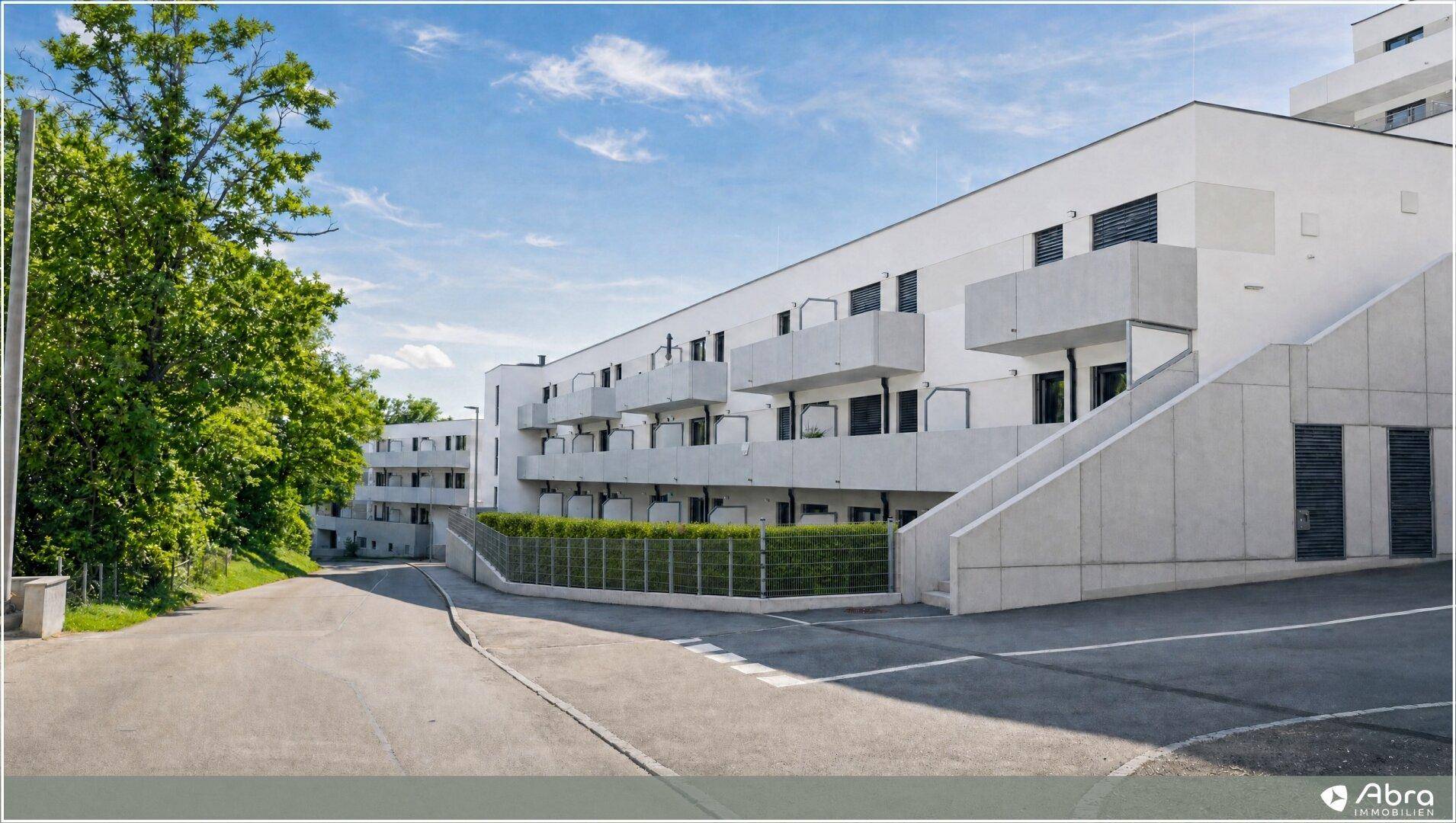 Moderne Wohnanlage mit klaren Linien, Balkonen und einer Zufahrt umgeben von Grünflächen.