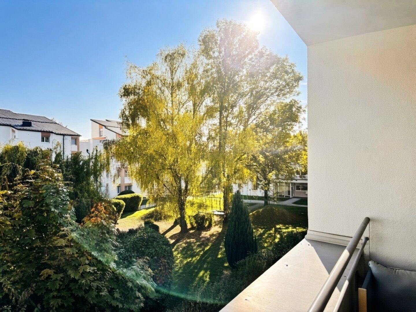 Sonniger Balkon mit weitem Blick auf grüne Bäume und die umliegende Wohngegend.