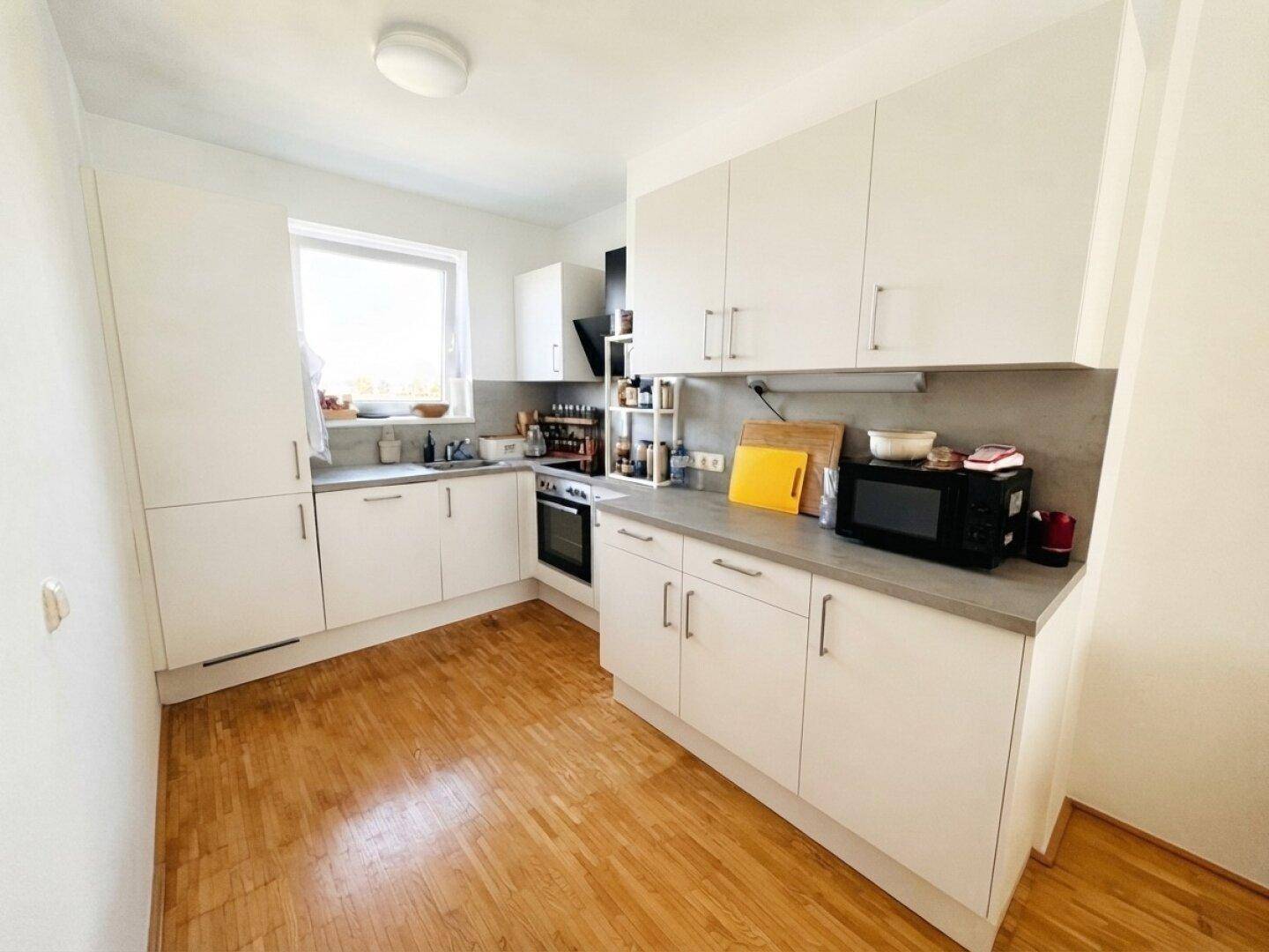 Funktionale Küche mit weißen Schränken, grauer Arbeitsplatte und Fenster für natürliches Licht.
