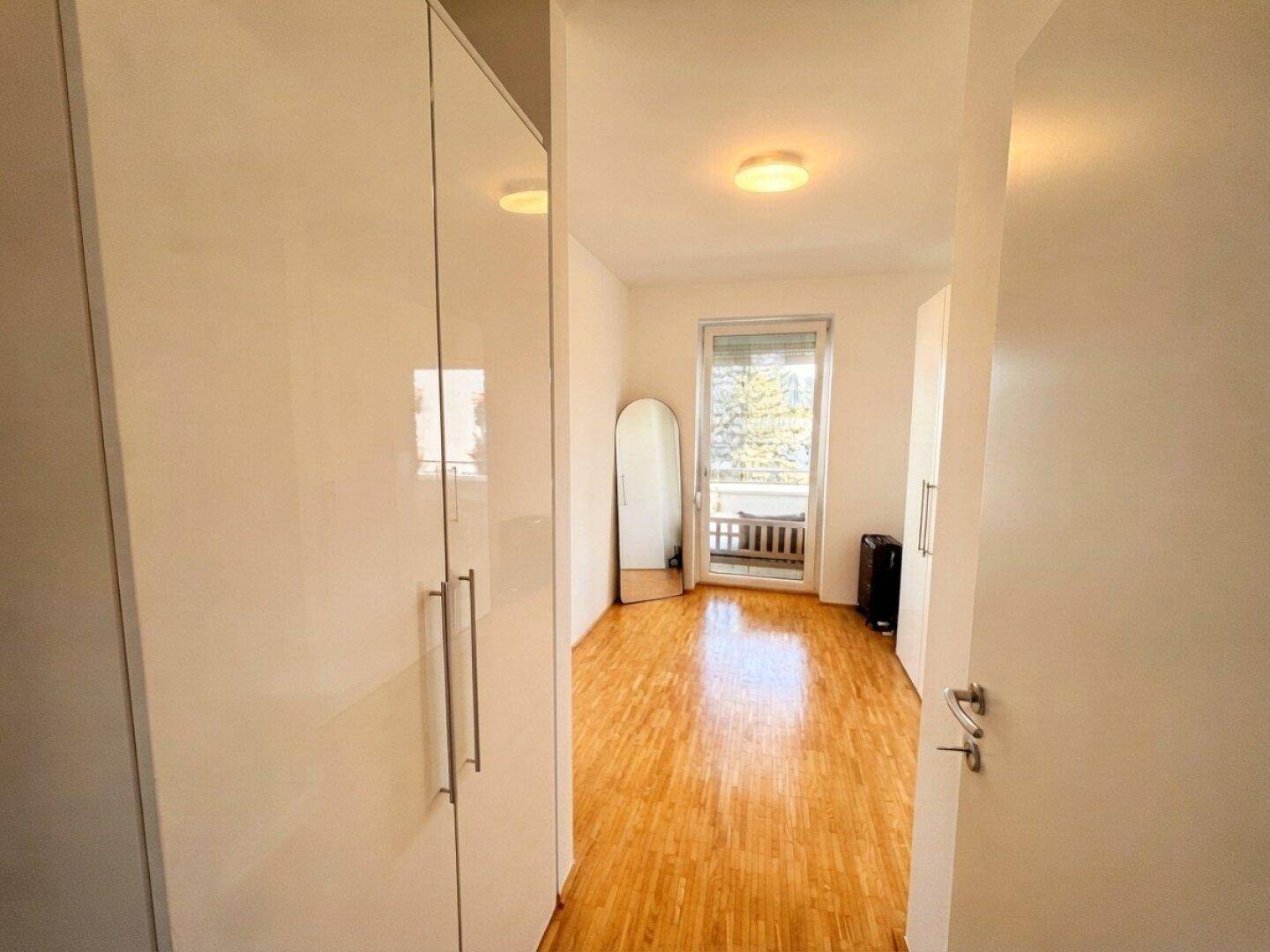 Geräumiges Schlafzimmer mit weißen Einbauschränken und direktem Zugang zum Balkon.