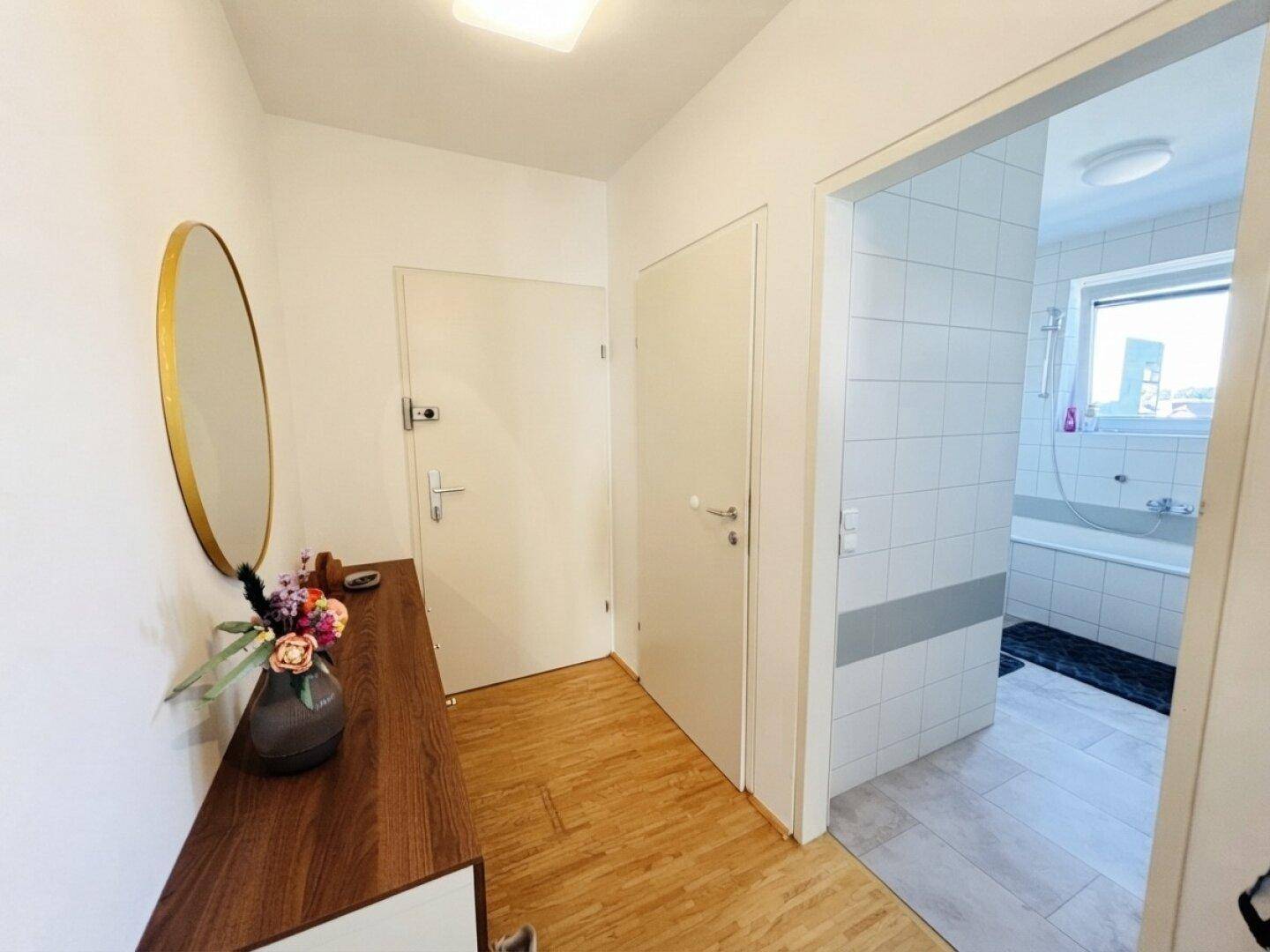 Heller Flur mit Holzkommode und Spiegel, der zum Badezimmer führt.