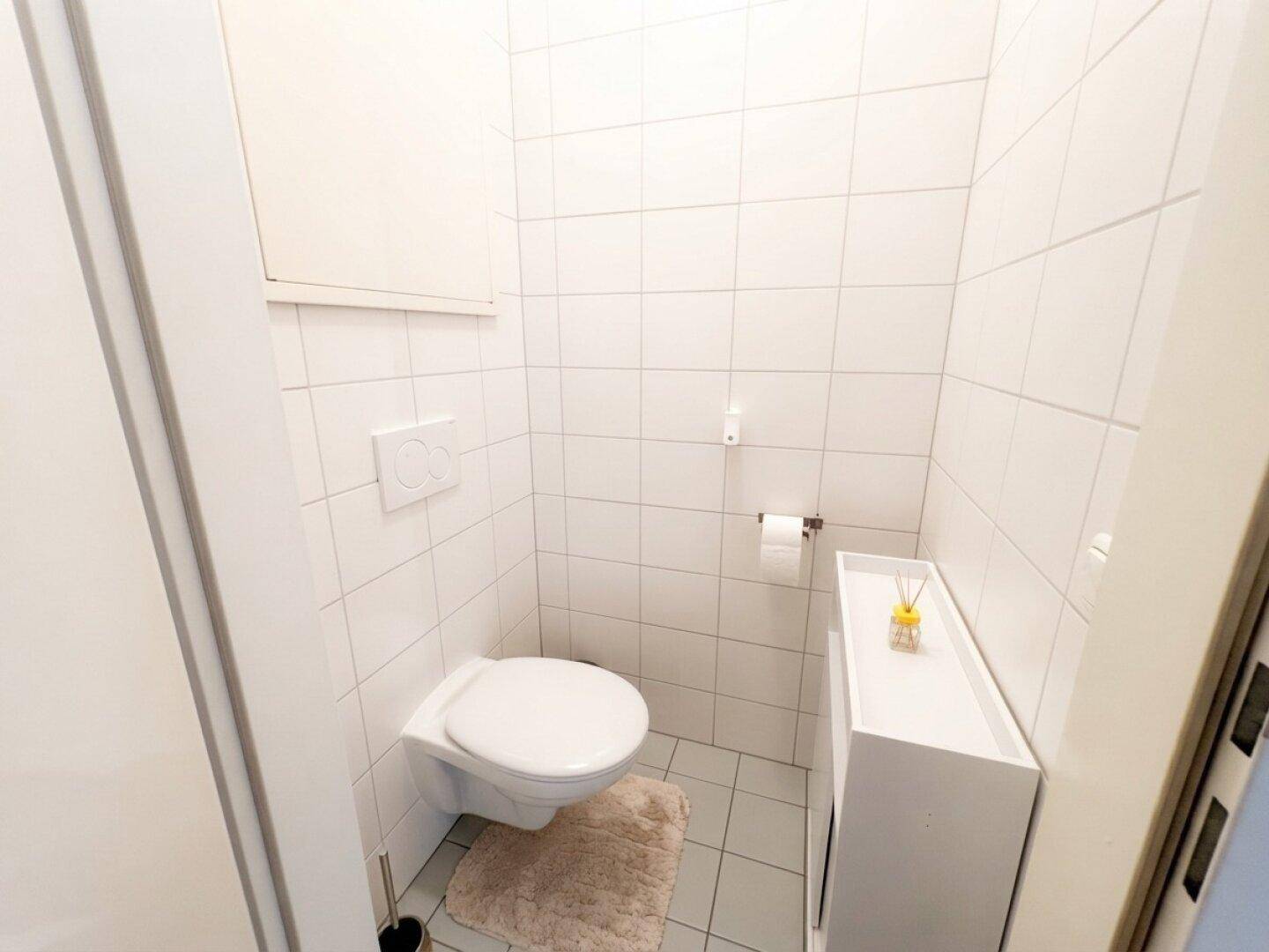 Kleines, hell gefliestes Gäste-WC mit wandhängender Toilette und kleinem Waschbecken.