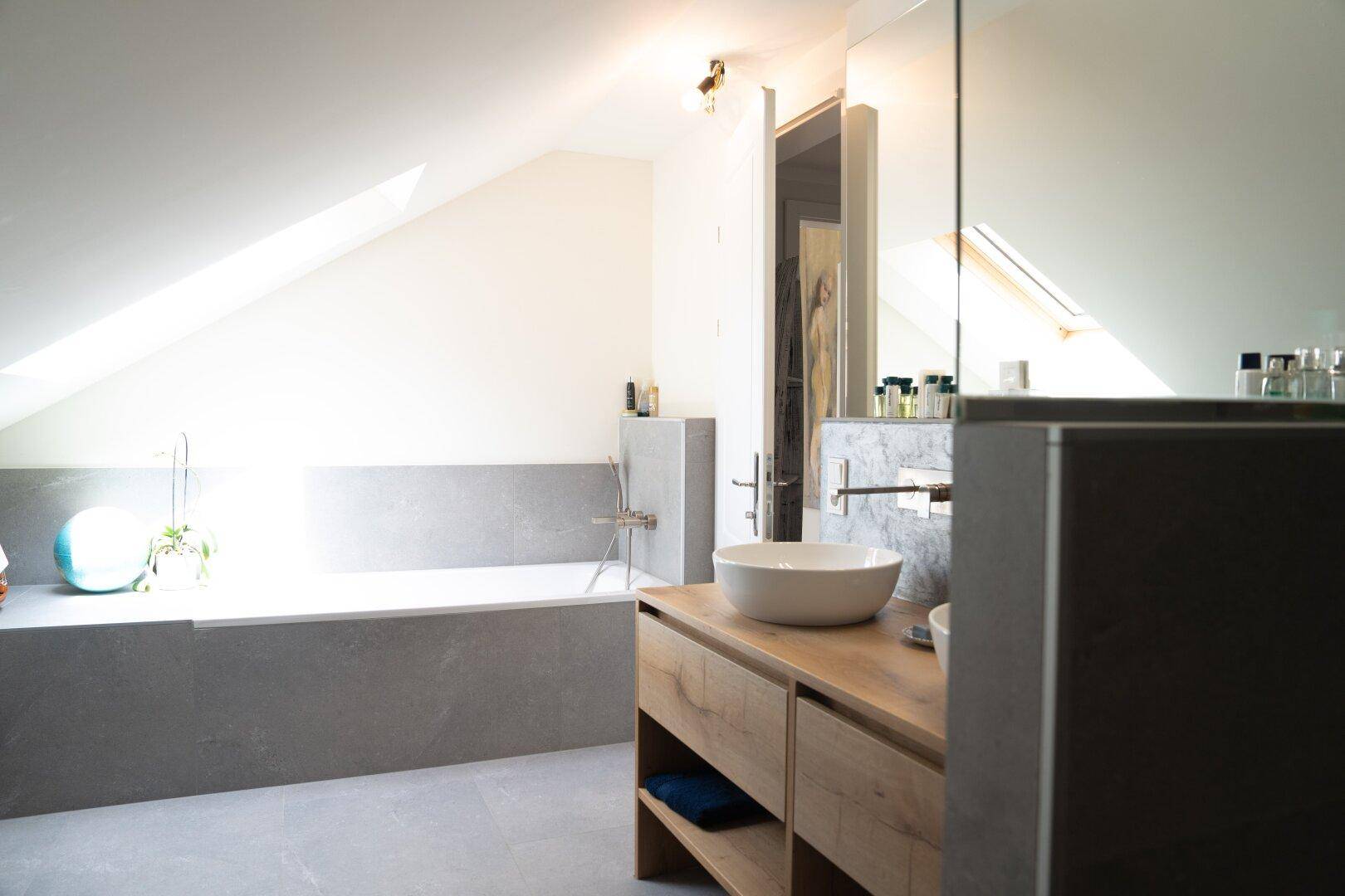 Modernes Badezimmer im Dachgeschoss mit Badewanne, Waschbecken und Dachfenster.