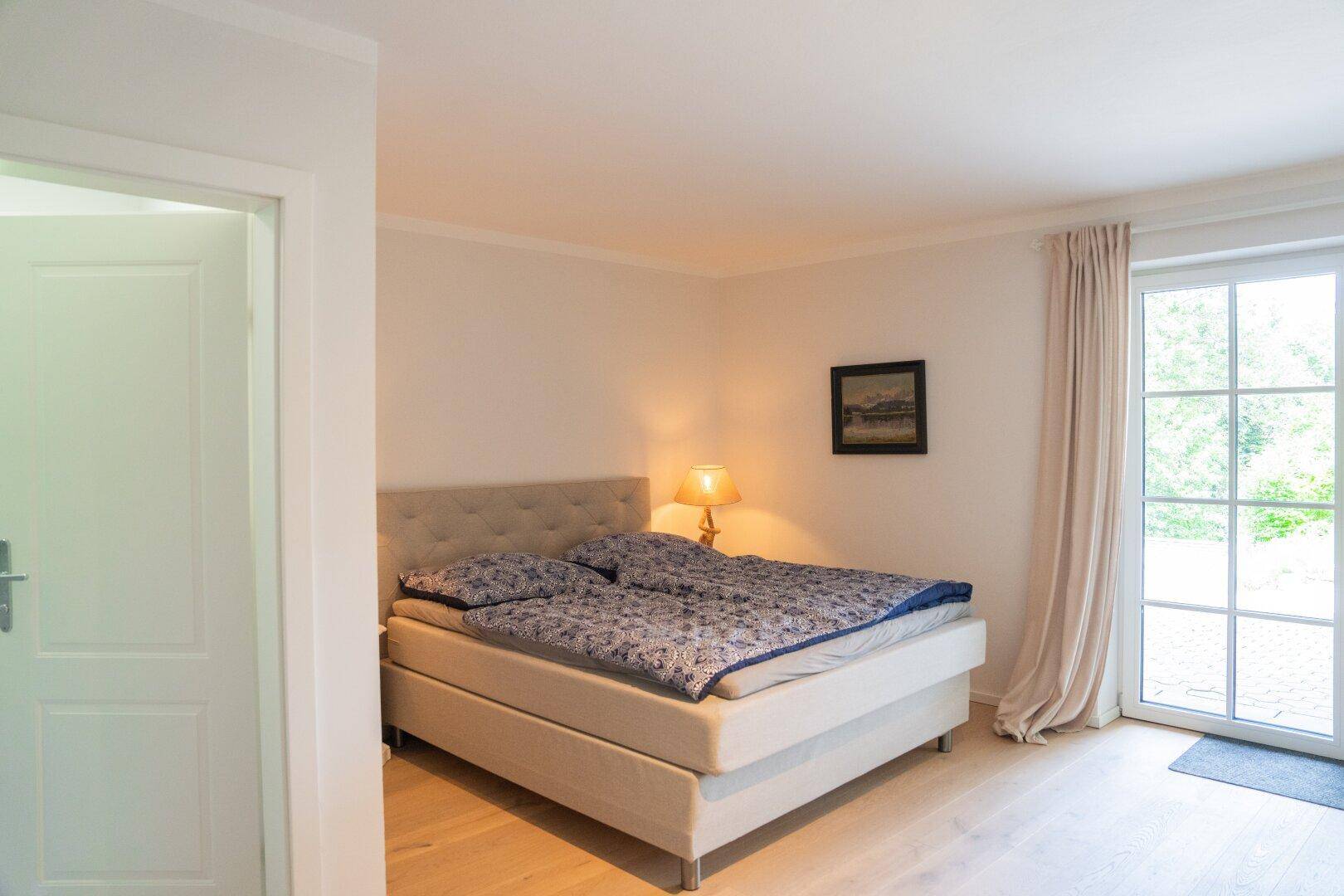 Gemütliches Schlafzimmer mit Doppelbett, Holzboden und Zugang zu einem Außenbereich.