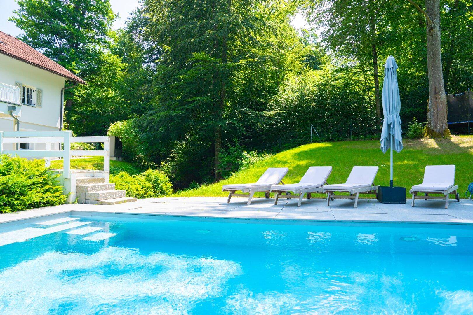 Entspannender Swimmingpool-Bereich mit Liegestühlen und Blick auf den bewaldeten Garten.