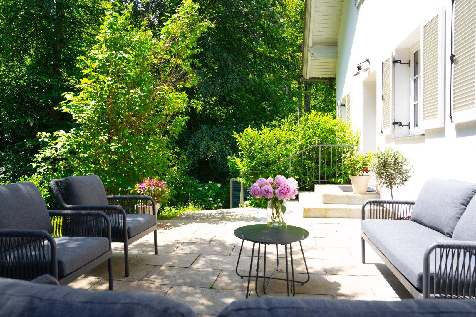 Gemütliche Terrasse mit bequemen Sitzmöbeln, umgeben von üppigem Grün und Bäumen.