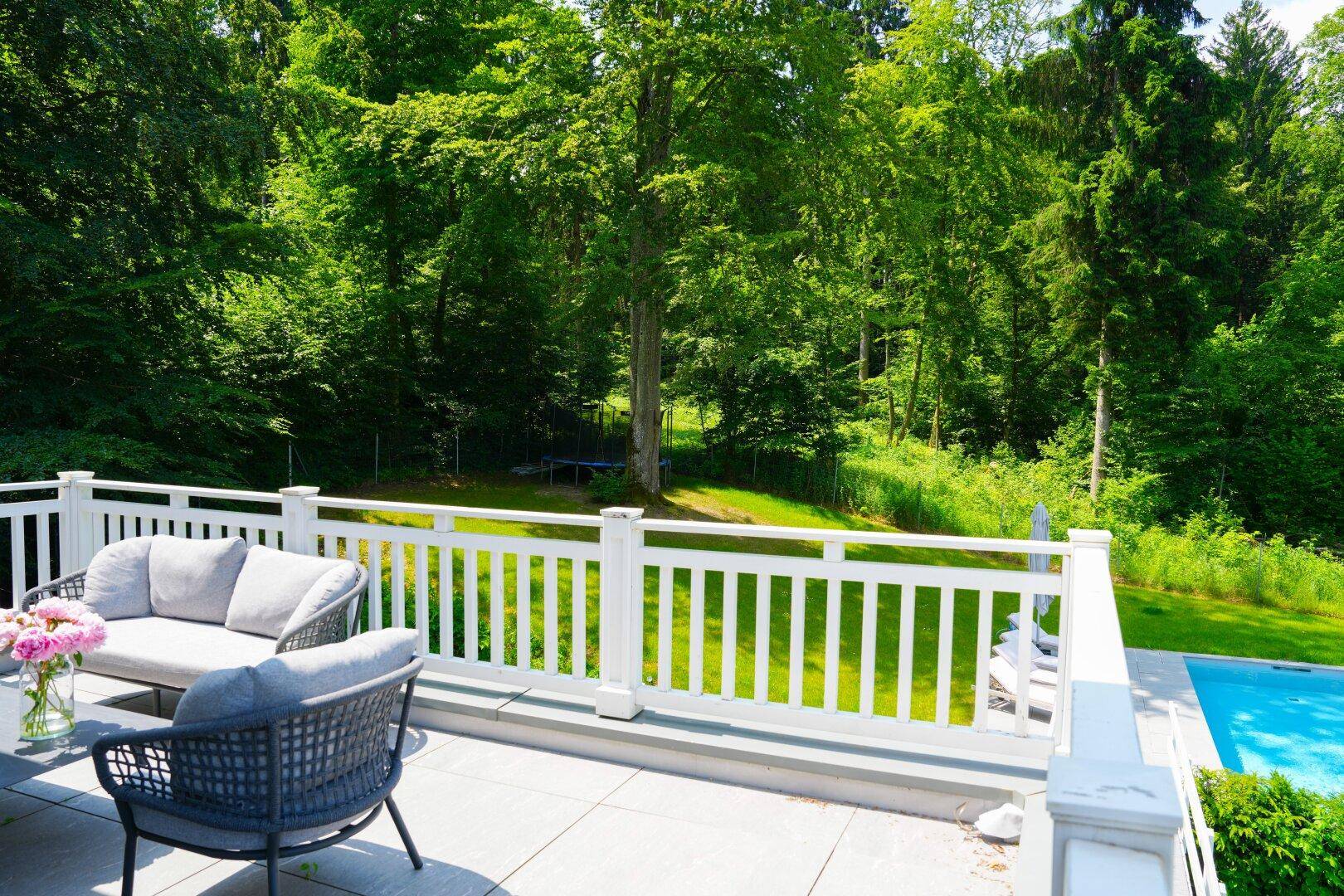 Terrasse mit Sitzgelegenheiten und Blick auf den Pool sowie den angrenzenden Wald.