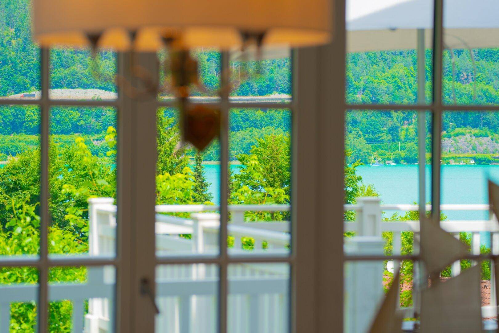 Durch die Sprossenfenster fällt der Blick auf den glitzernden See und die grüne Landschaft.