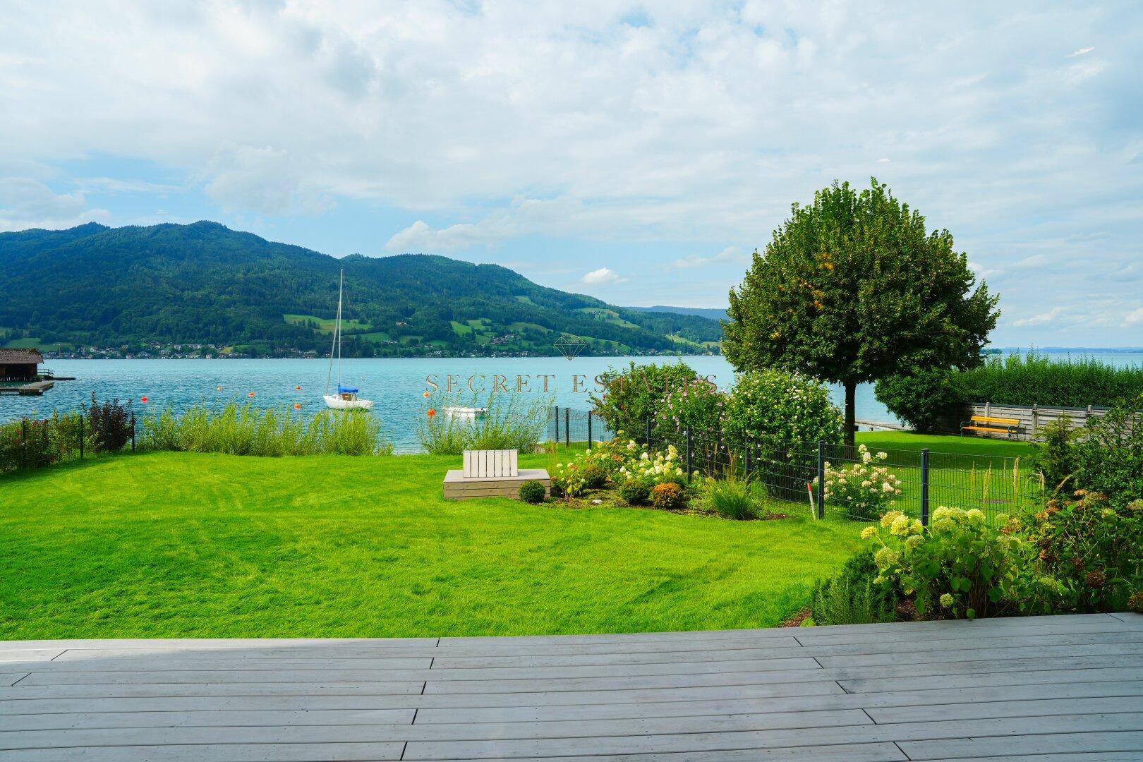 Gepflegter Garten mit Rasenfläche, Holzterrasse und direktem Zugang zum See.
