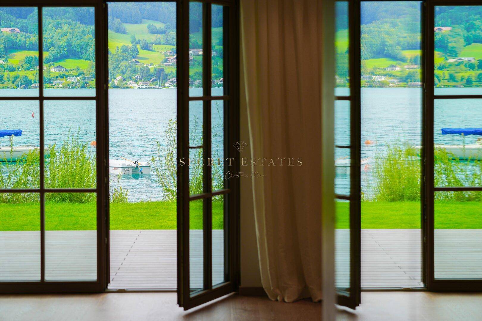 Große Fensterfront mit Blick auf den See und die umliegende grüne Landschaft.