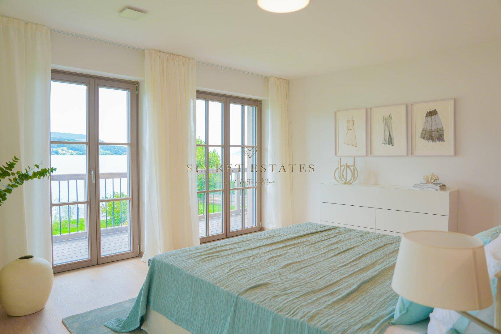 Schlafzimmer mit Seeblick, Balkonzugang und hellem Holzboden.