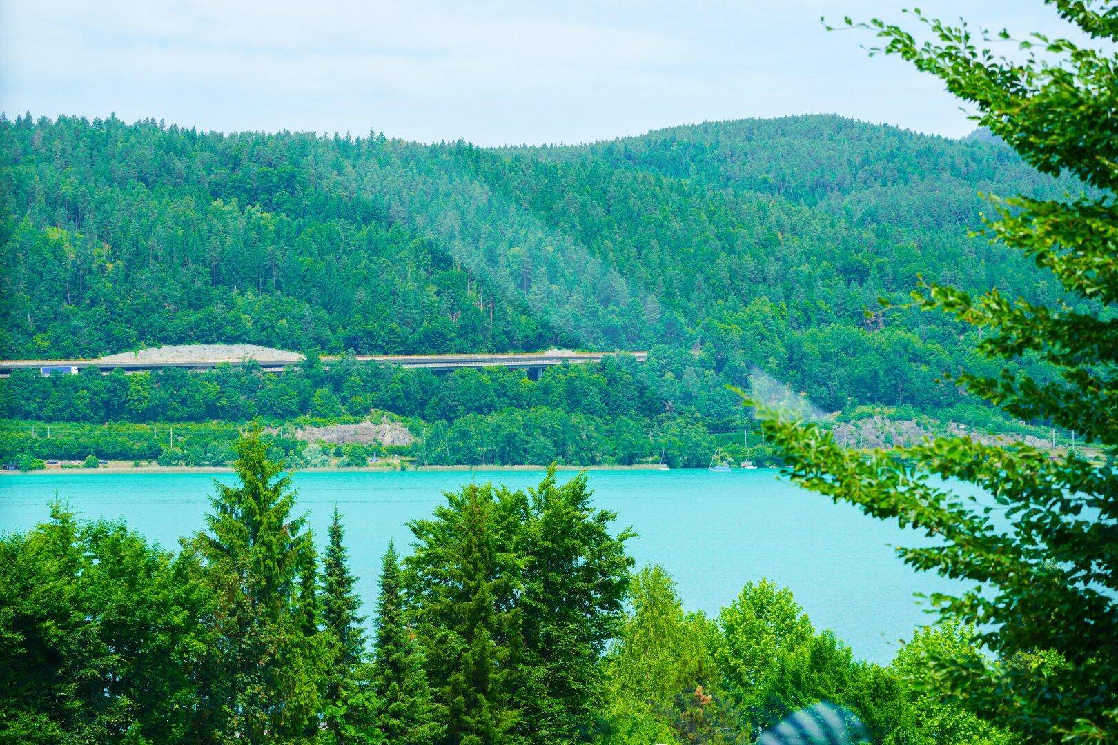Weitläufiger Blick auf den türkisblauen See und die bewaldeten Berge.