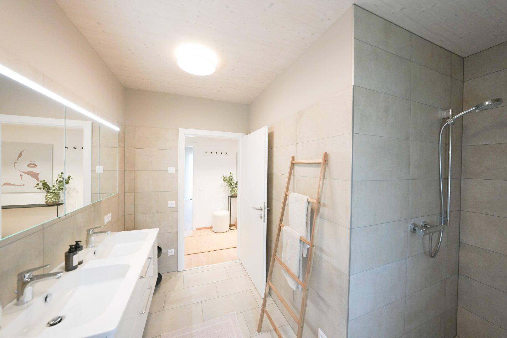 Modernes Badezimmer mit Doppelwaschbecken, großer Dusche und hellen Fliesen.