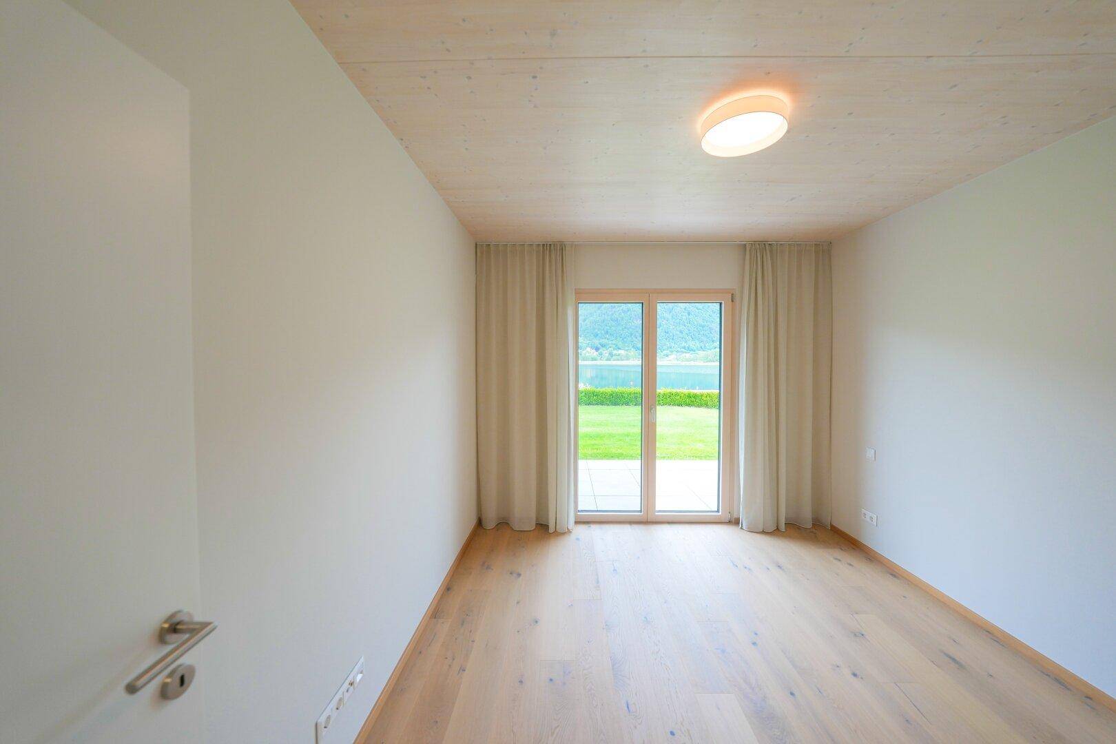 Leerer Raum mit Holzboden und großen Fenstern mit direktem Seeblick.