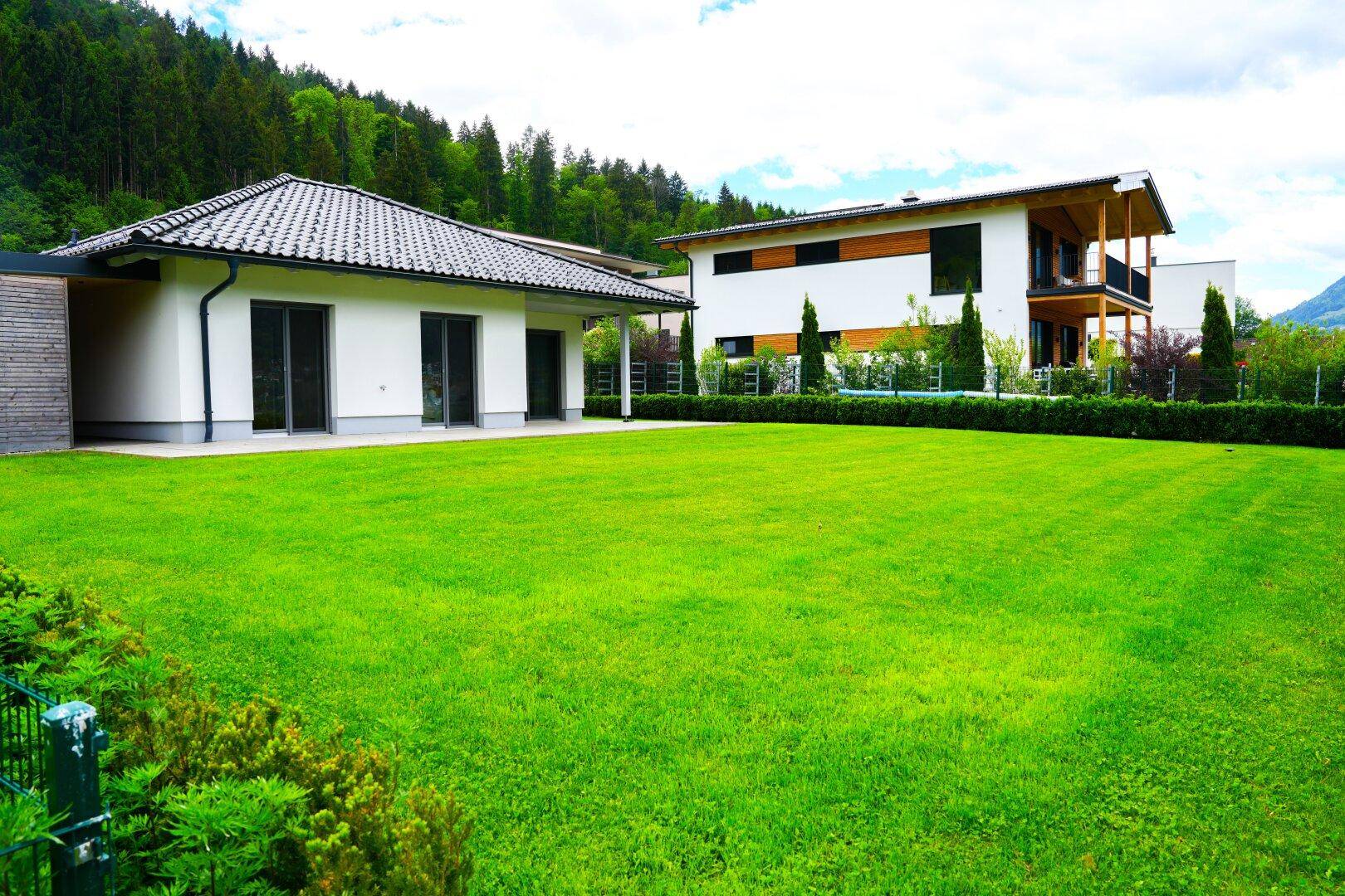 Zwei moderne Häuser mit großzügiger Rasenfläche und Bergblick in ländlicher Umgebung.